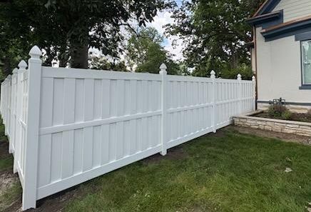 White vinyl shadowbox fence installed by Guarantee Fence Company. There is green grass and trees all around the fence.